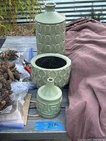 Set of three green ceramic decorative vases of various shapes and embossed geometric patterns on a table outside.
