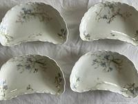 Photo of four kidney-shaped sauce dishes with floral decoration placed on a white cloth background.