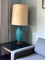 Full view of the lamp placed on a glass top side table next to a light gray upholstered sofa, showing the lamp's height and proportions.