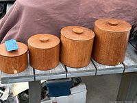 Four wooden canisters of varying sizes in a row showing their lids and wood grain.
