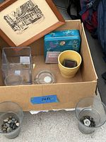 Box containing clear glass vases, yellow pot, ashtray, blue tin container, and framed artwork.