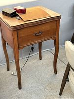 Vintage oak sewing machine cabinet with decorative drawer handle and curved legs, showing overall condition and wood finish.