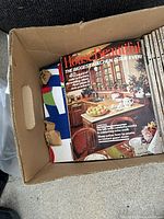 Photo showing multiple House Beautiful magazines in a cardboard box, focusing on an issue featuring a kitchen on the cover.