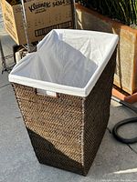 Full view of dark wicker hamper with white liner inserted inside, rectangular shape, taken in daylight.