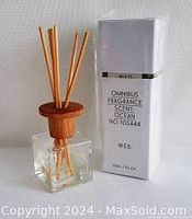 Clear glass fragrance diffuser bottle with wooden top and reeds alongside original white box packaging showing product details.