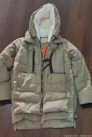 Front view of light olive green OROLAY thickened down jacket with zipper and pockets visible, laid flat on floor