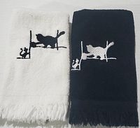 Two folded hand towels, one white and one dark navy, with stitched cat and mouse patterns, showing fringed edges.