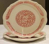 Two scalloped edge red transferware dinner plates displayed side by side showing full design and shape.