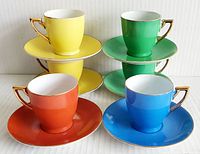 Front and side view of six brightly colored demitasse cups with matching saucers in yellow, green, orange, and blue. Cups have gold trim and handles. Arranged in two stacks of three with plates below.