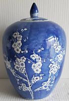 Front view of large vintage blue and white ginger jar with lid on top, showing floral design in white on deep blue background.