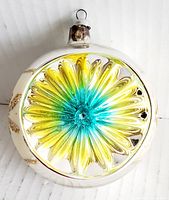 Front close-up showing concave reflective flower center in yellow and turquoise blue highlights, glass ornament with metal cap and loop