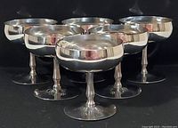 Front angled view of all six stainless steel vintage champagne coupe/dessert cups grouped together on black background.