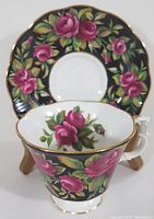 Tea cup and saucer with floral pink rose pattern on black background with gold trim visible from front