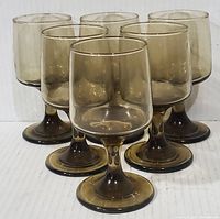 Front angle view of six smokey brown glass goblets arranged in two rows showing translucent brown color, solid stems and round bases