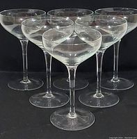 Group of six tall vintage French crystal champagne coup glasses arranged in two rows on a black background showing clear, shallow bowl shape and slender stems.