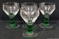 Set of four goblets with emerald green stems and clear beveled bowls, displayed on black background.