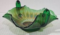 Front angled view of green carnival glass bon bon dish showing the stippled rays pattern and double handles.