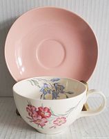 Cup with floral decoration in front of plain pink saucer