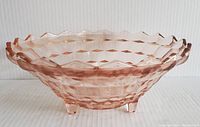 Pink Depression glass footed bowl with Cubist geometric pattern, scalloped edge, and three feet, shown from a side angle.