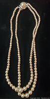 Full view of double strand pearl necklace laid flat on black background.