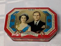 Octagonal commemorative tin with portrait of Queen Elizabeth II and Prince Philip on the lid, red background, blue and gold decorative borders, and heraldic shields on the sides.