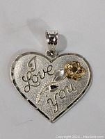 Close-up of the front side of the pendant showing the engraved 'I Love You' text and gold flower detail.