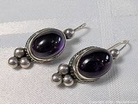 Pair of vintage sterling silver drop earrings with oval cabochon amethyst and silver bead accents, displayed on fabric background.