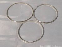 Top-down photo showing all three silver bangles arranged on a reflective surface.