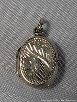 Front view of the sterling silver oval locket showing the detailed carved floral and leaf design and bail loop.