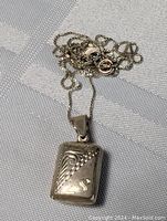 Sterling silver rectangular carved locket with 19-inch sterling silver box chain, laid out showing detailed carving and chain clasp.