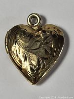 Front view of the gold tone heart-shaped locket pendant with carved floral scroll design.
