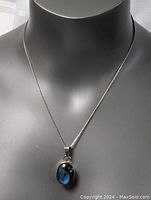 Sterling silver necklace displayed on bust with 18-inch box chain and oval blue pendant in unknown setting.