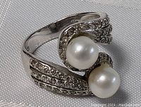 Close-up front angle of the sterling silver ring showing two white round pearls and the small clear stones on the band in a crossover design.