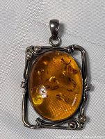 Front view of the vintage amber pendant showing the oval amber stone with inclusions and the sterling silver frame with twisted wire and bead accents.