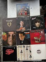 Photo showing eight vinyl record albums arranged on floor including Mormon Tabernacle Choir, Itzhak Perlman, Mosaic Gary Wright, Jesus Christ Superstar, Barry Manilow, Fame, Andy Williams, and a close-up woman's face album.