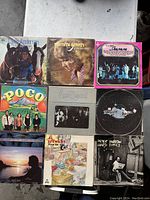 Top view of nine vintage vinyl record album covers laid out on a flat surface showing artwork and artist names