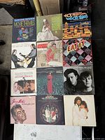 Photo showing twelve vinyl record albums arranged in 3 rows of 4, various cover art styles and artists.