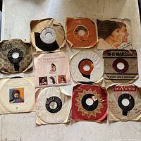 Full view of all 11 vintage 45 RPM vinyl records laid on surface, shown in sleeves or protective paper.