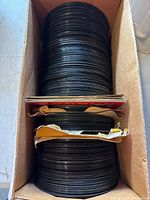 Top view of stacked vintage black vinyl records in a cardboard box, some visible record labels and torn sleeves at top.