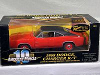 Front and side view of boxed 1968 Dodge Charger R/T die cast model, showing red body and black vinyl roof inside clear display box with worn edges.