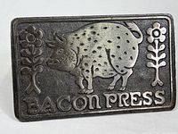 Close-up of the front embossed cast iron surface featuring a pig and floral motifs with text 'BACON PRESS'.