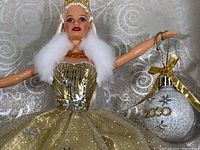 Close-up of Barbie doll head and upper torso showing gold dress bodice, white faux fur collar, and holding a 2000 ornament