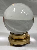 Front view of the clear crystal ball on gold painted wood stand showing the reflective surface and red velvet lining on top of the stand.