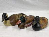 Three carved wood and hand-painted decorative duck decoys shown from the side on a white background.