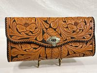 Front view of the hand tooled leather purse showing floral designs and silver-tone twist lock closure.