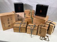 Group photo of ten wood boxes of various sizes and finishes, tied or secured with woven ribbons. Some boxes have Japanese script on lids and sides, two black boxes have red diamond details.