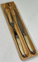 Full view of Laguiole carving knife and fork, showing light cream handles and wood tray with brand logo