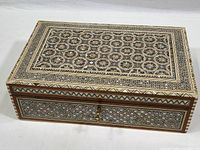 Full view of closed rectangular wooden jewelry box with ornate shell mosaic top and front, lock and key visible at front.