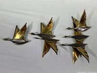 Three polished brass flying geese sculptures arranged to show overall size and formation on white background