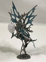 Full view of the metal fairy sculpture showing body and glittered wings, standing on tree branch base.